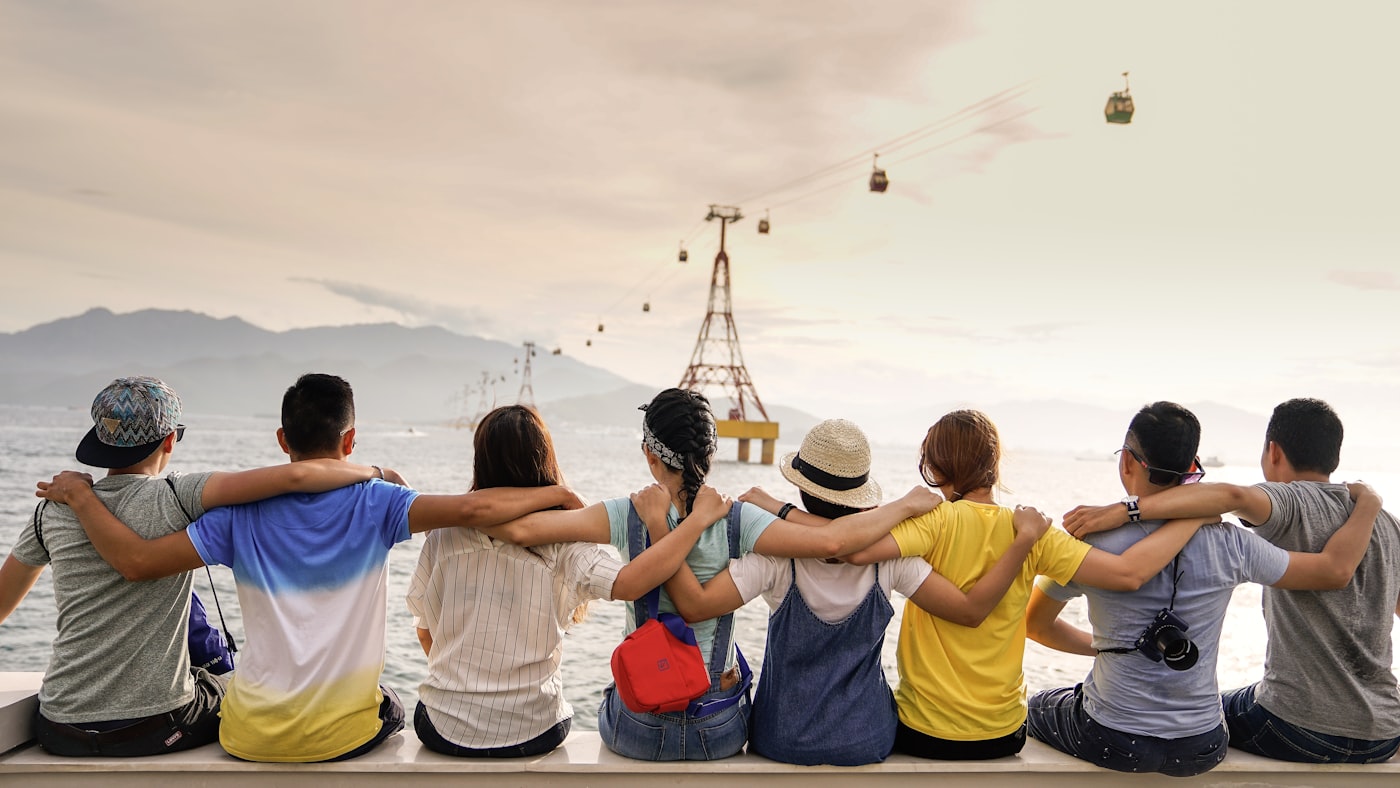 A group of friends with their arms around each other watching cable cars over the water.