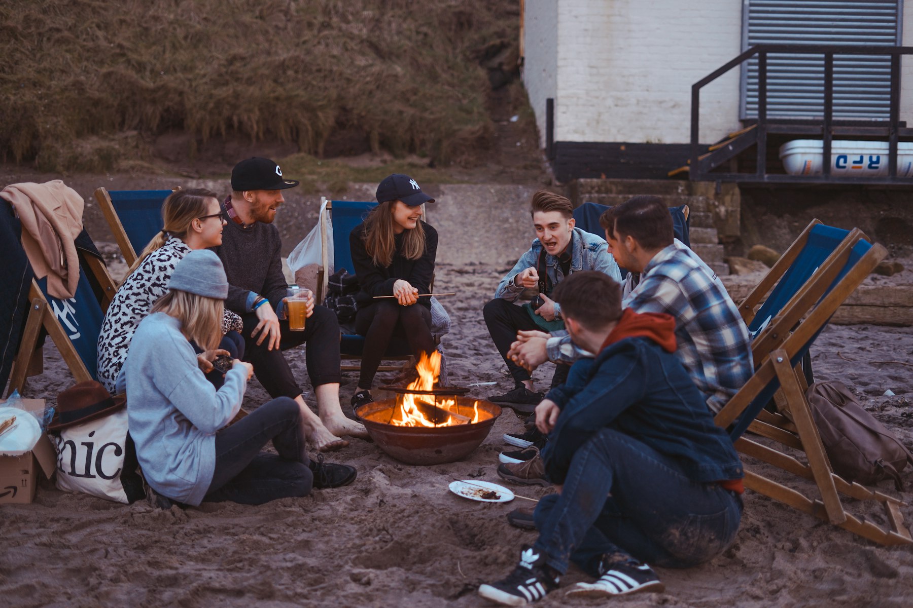 A group of friends gathered around a campfire on the beach at dusk.